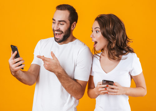 presenečen mlad par s telefonom, oranžno ozadje